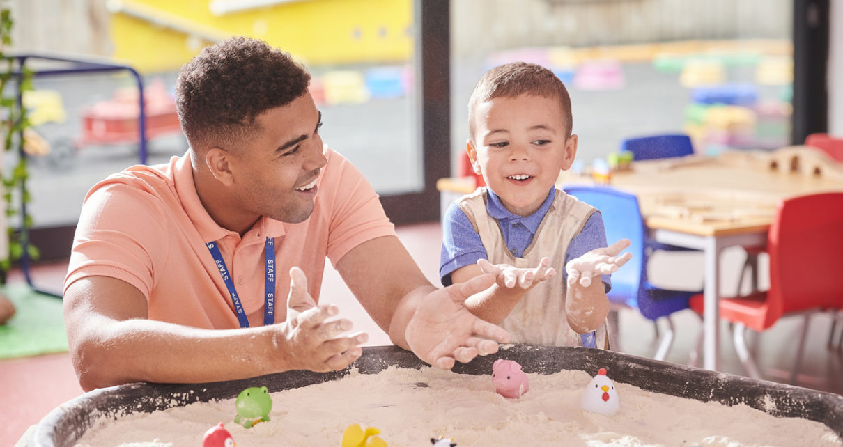 Nursery teacher with student exploring the sandpit.