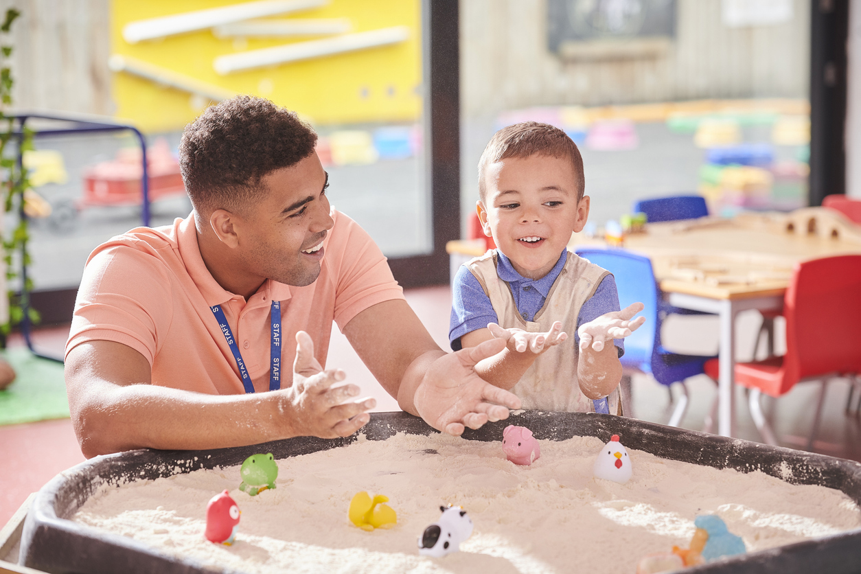 Nursery teacher with student exploring the sandpit.